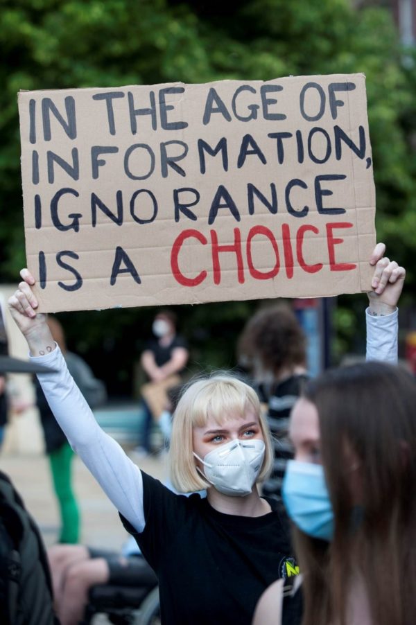 Photograph of a protestor holding a placard that reads: 'In the age of information, ignorance is a choice'.
